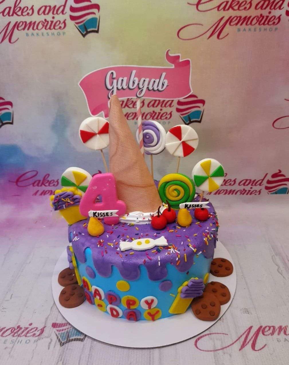 Colorful candy-themed birthday cake with purple and blue icing, lollipops, ice cream cone, and cookies.