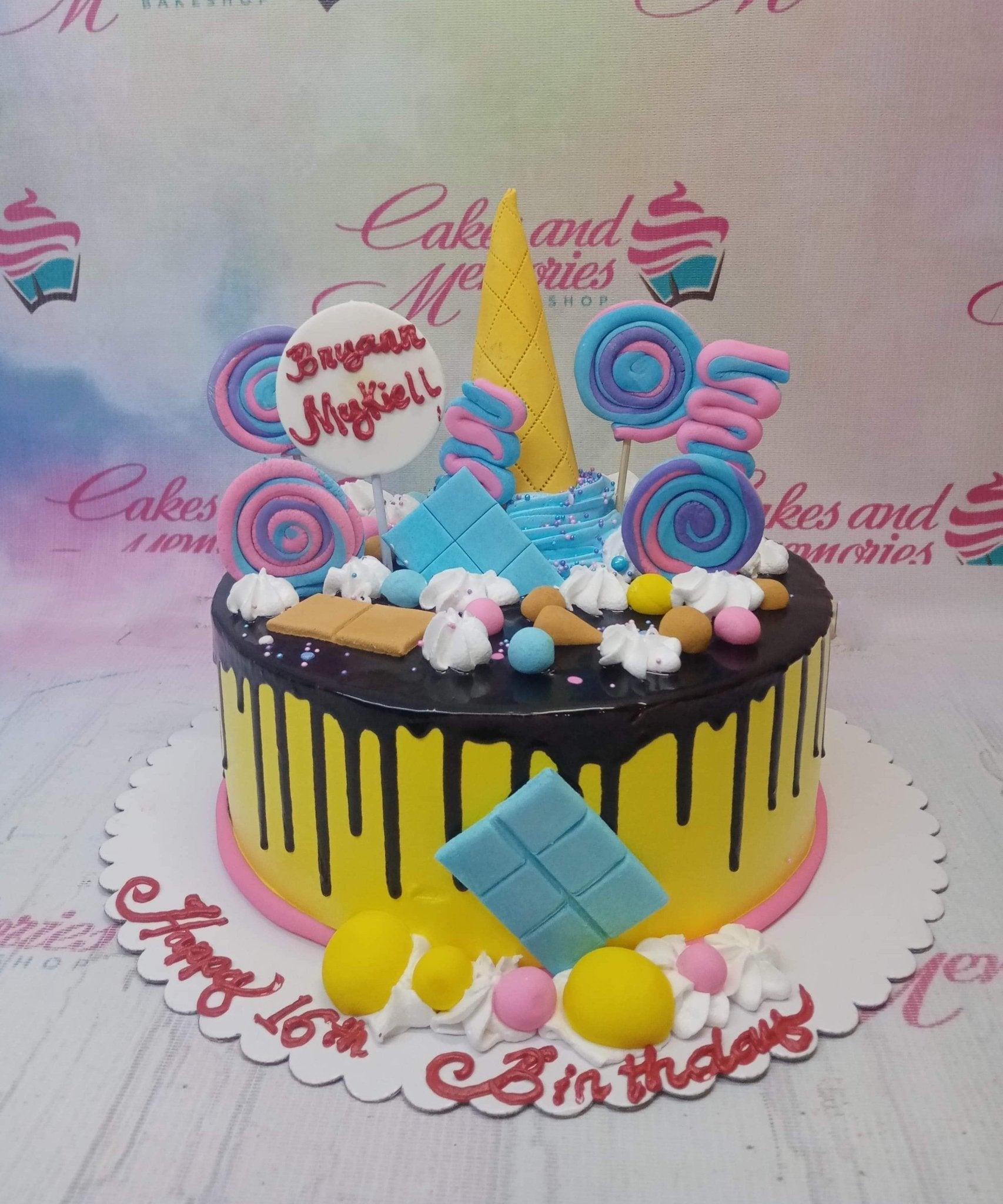 Yellow birthday cake with chocolate drip, colorful fondant lollipops, a yellow ice cream cone topper, and blue chocolate bar accents.