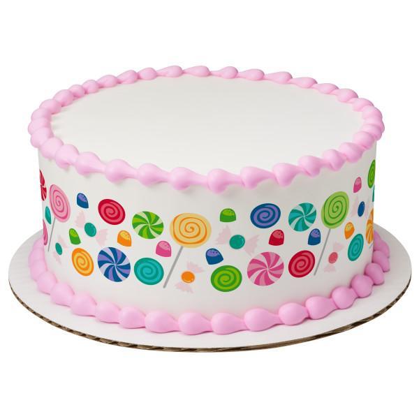 White round cake with pink piped icing borders and colorful candy and lollipop printout designs on the sides.