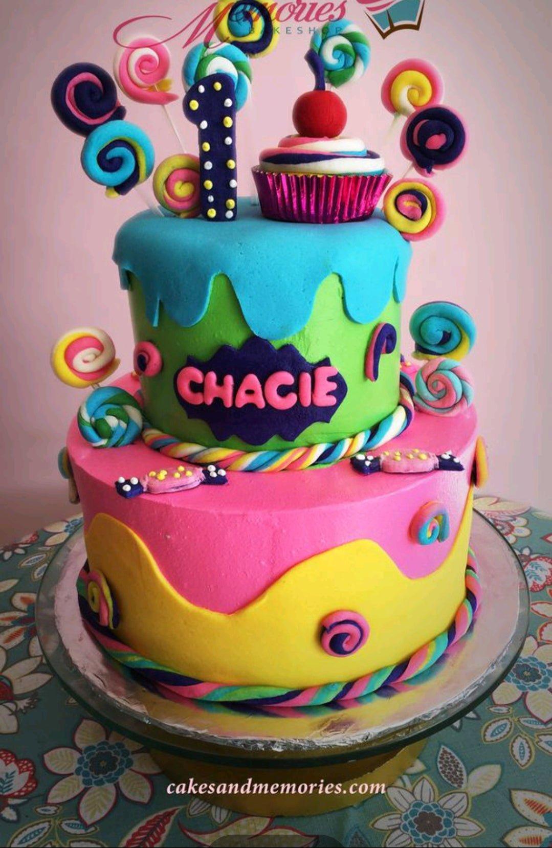 Colorful 2-tier candy themed birthday cake with fondant lollipops, a cupcake topper, and a number one candle.