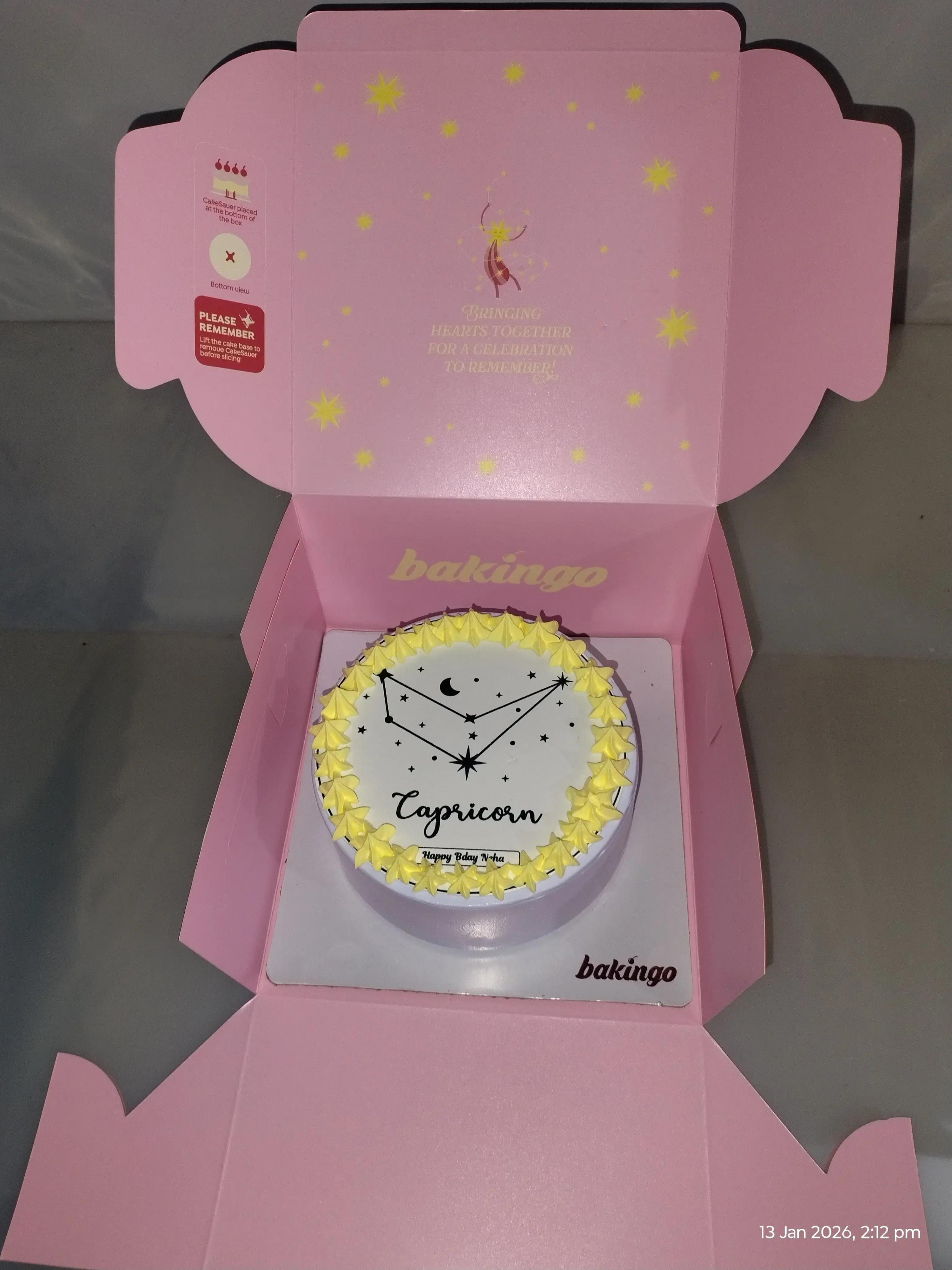 White bento cake with yellow icing rosettes and a black Capricorn constellation design on top.