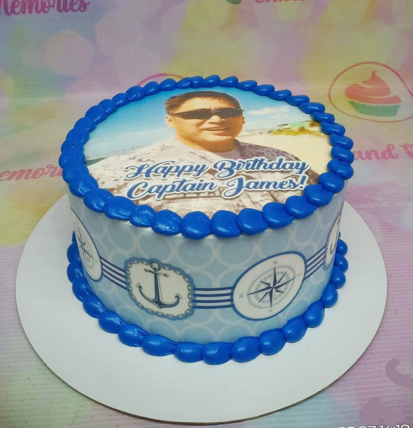 Blue and white nautical themed birthday cake with a photo print of a captain and blue icing borders.