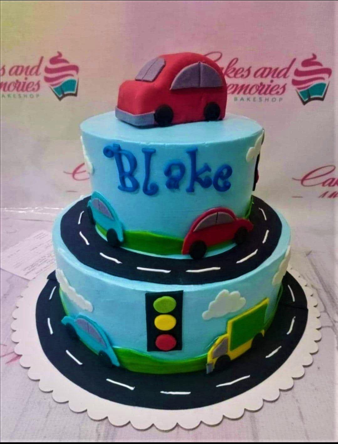 Two-tier light blue fondant car themed birthday cake with a red 3D car topper, traffic light, and road designs.