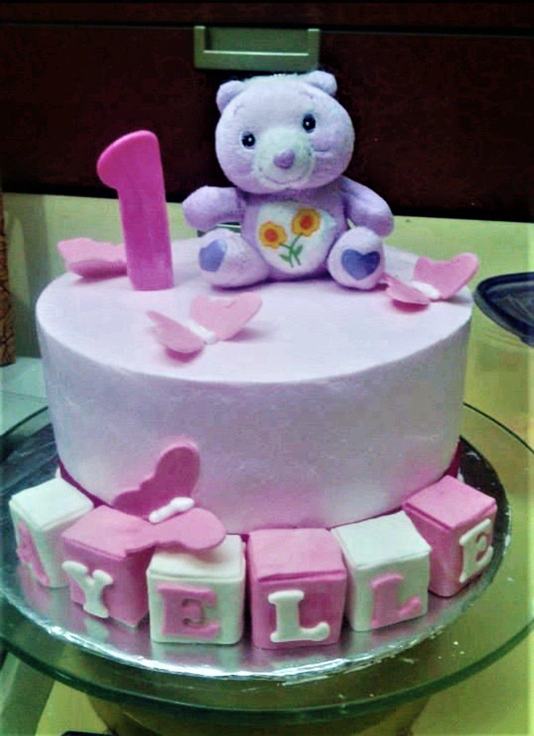 Light purple Care Bear birthday cake with pink butterflies and name blocks for Elle.
