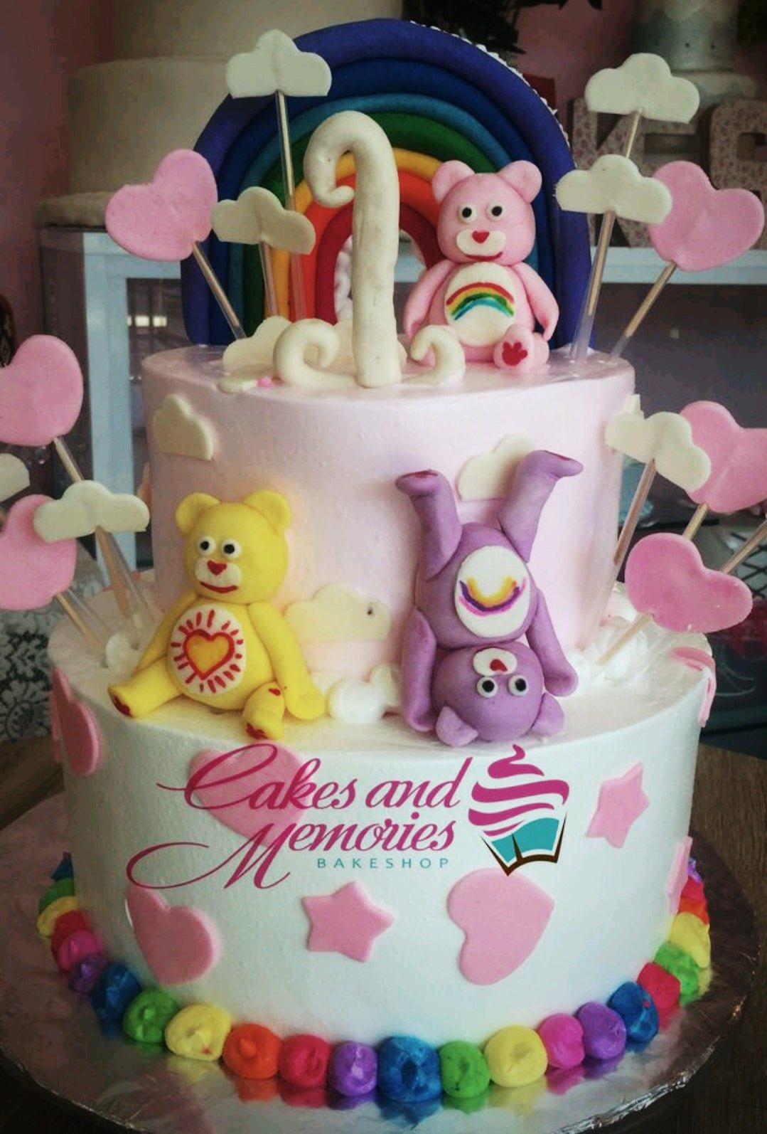 Two-tier pink and white Care Bears birthday cake with fondant rainbow, bears, and heart decorations.