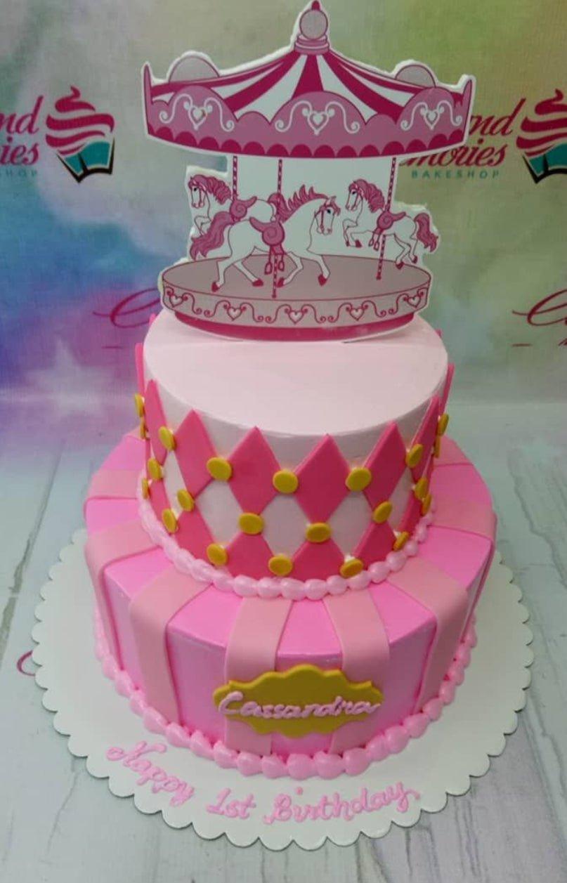 Pink 2-tier carousel themed birthday cake with pink and light pink stripes, diamond patterns, and a carousel horse printout topper.