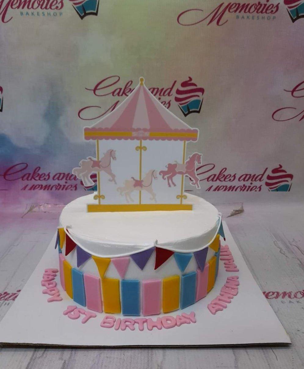 White 1-tier carousel birthday cake with colorful fondant bunting and vertical stripes.