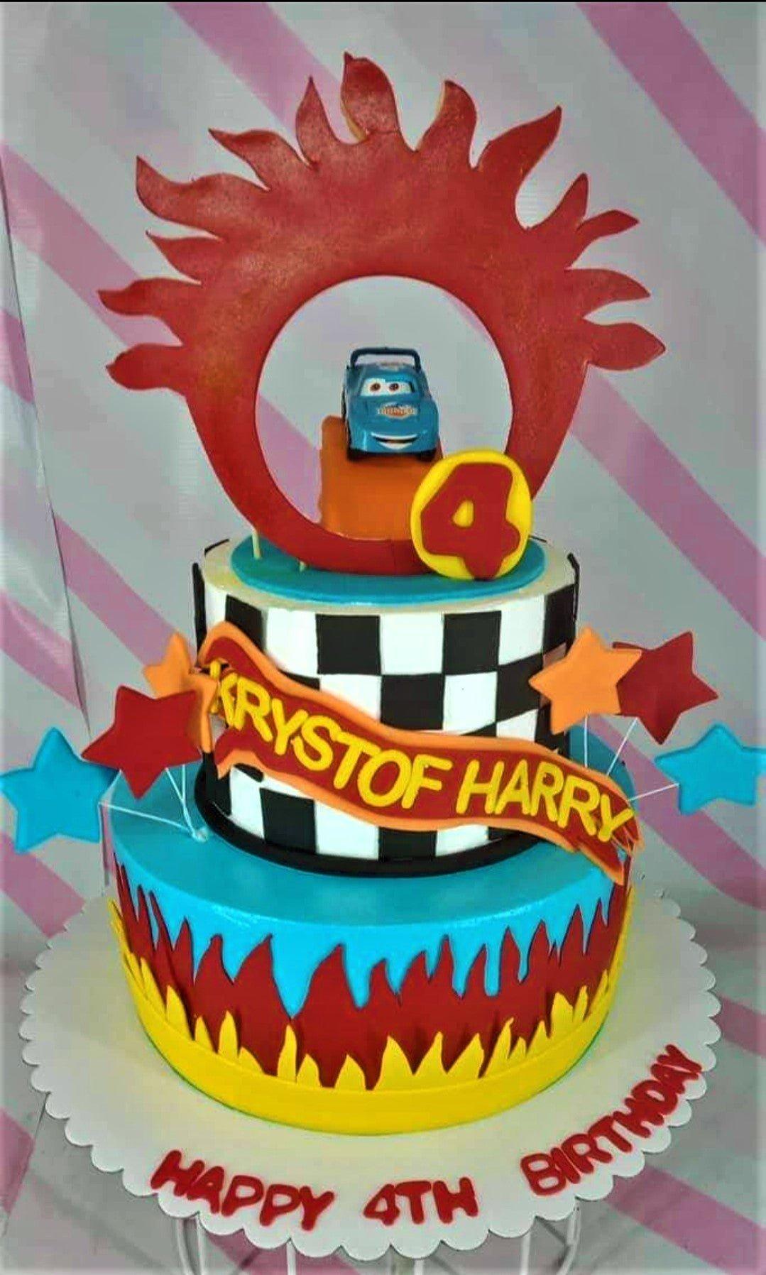Two-tier Cars themed birthday cake with a blue toy car, checkered pattern, and red flame designs for Krystof Harry's 4th birthday.