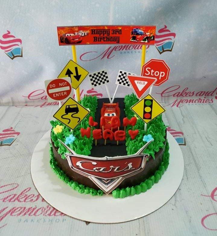 Disney Cars themed chocolate cake with Lightning McQueen topper, road signs, and green grass icing for a 3rd birthday.