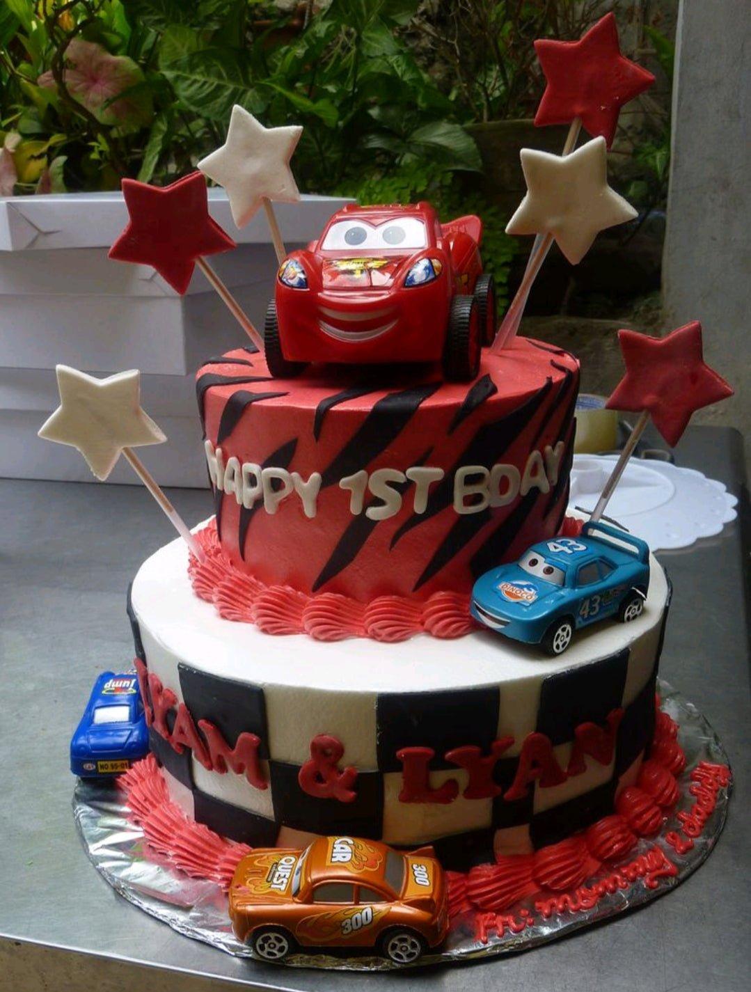 Two-tier Cars themed birthday cake with Lightning McQueen toy topper, red and black tiger stripes, and checkered flag pattern.