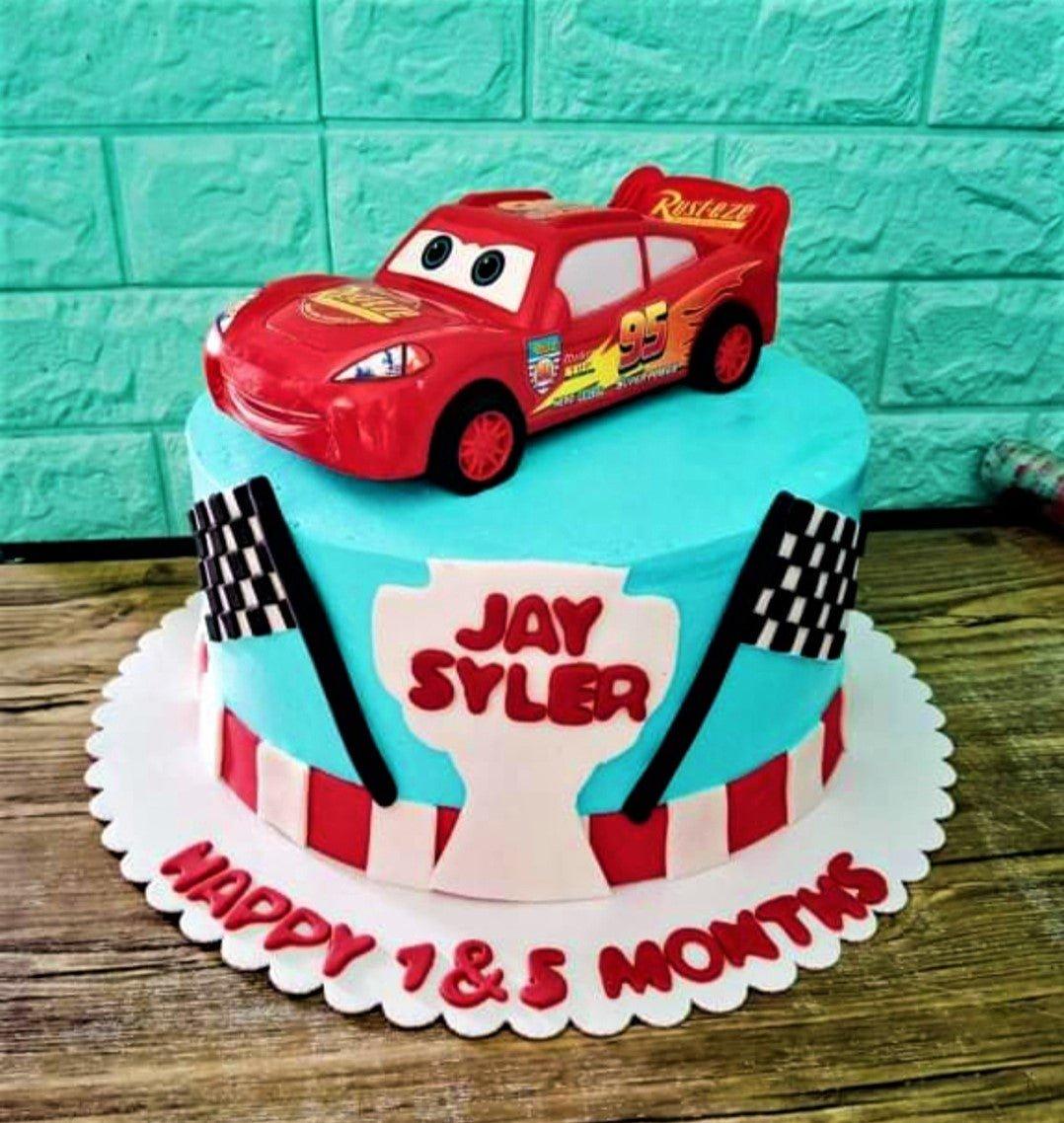Light blue Cars themed birthday cake featuring a Lightning McQueen toy topper and checkered racing flags.