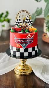 Red Cars themed birthday cake with Lightning McQueen and Mater toppers, checkered racing flag pattern, and a custom logo message.