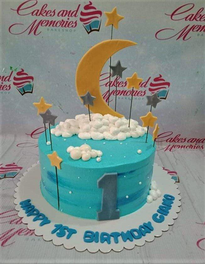 Light blue celestial birthday cake with a large yellow crescent moon, stars on sticks, and white icing clouds.