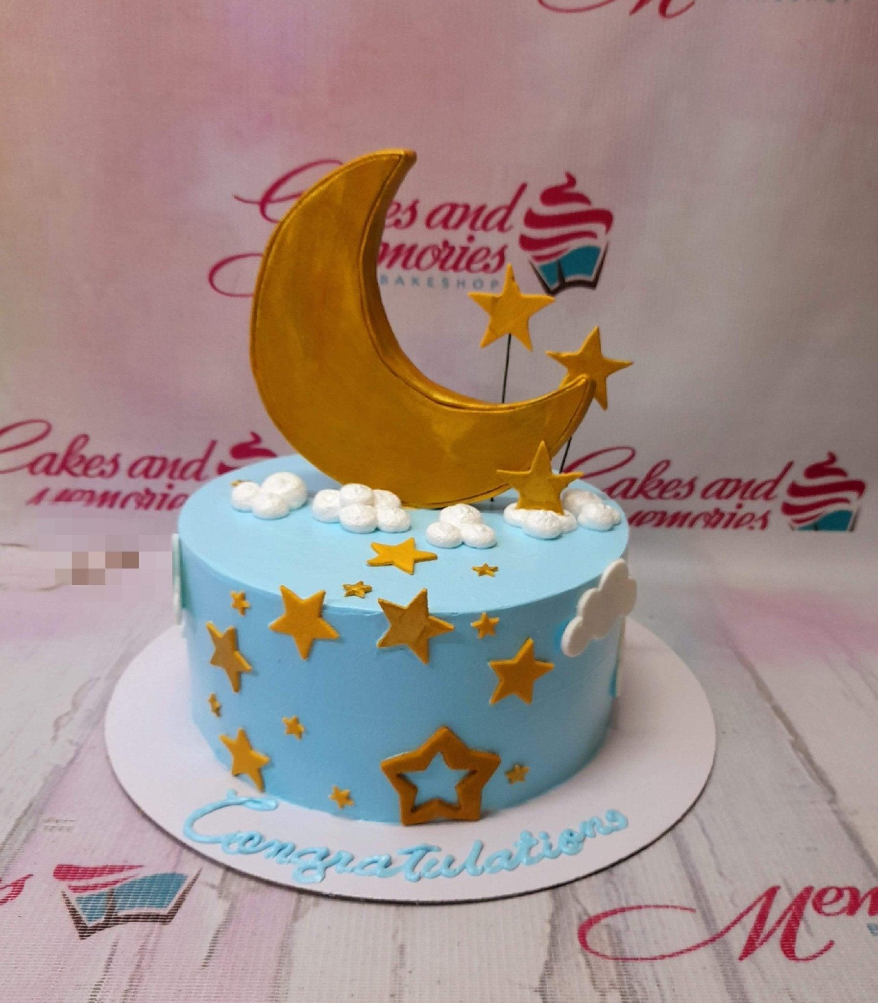 Light blue celestial cake with a large gold crescent moon topper, white fondant clouds, and gold stars.