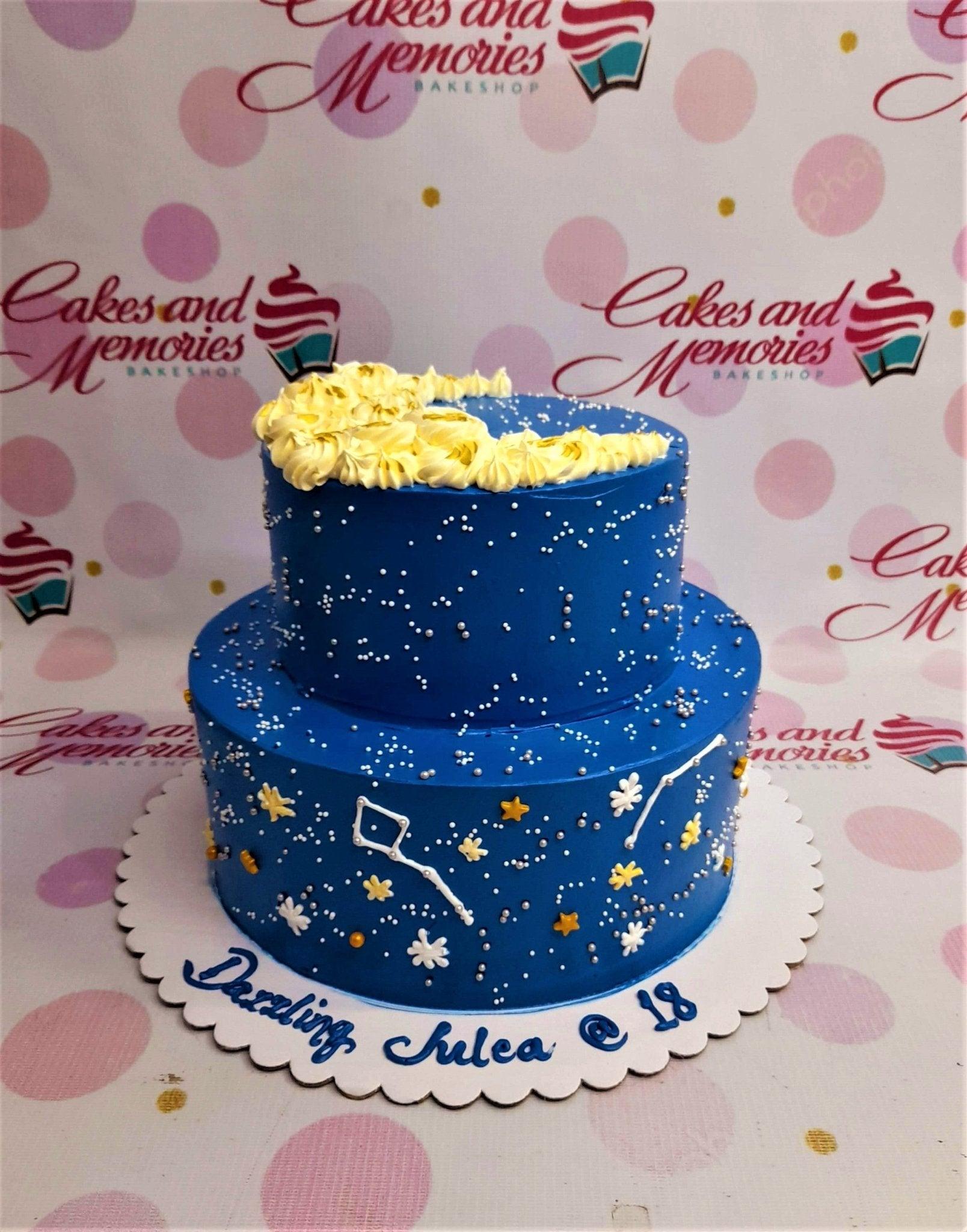 Two-tier navy blue celestial cake with a yellow crescent moon icing topper, white constellations, and gold stars.