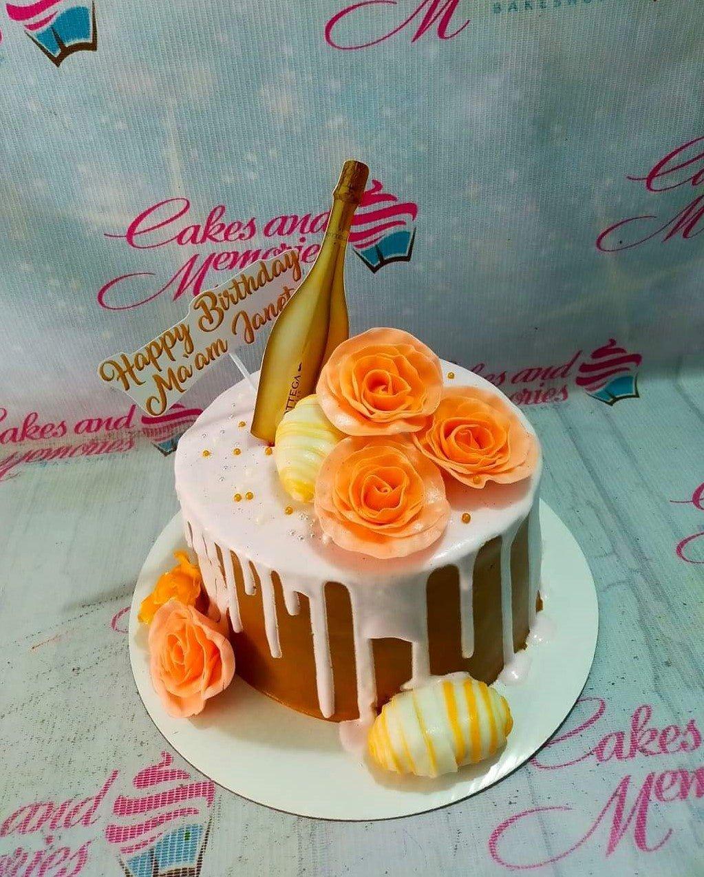White soft-icing cake with brown chocolate drip, orange roses, and a gold champagne bottle topper.