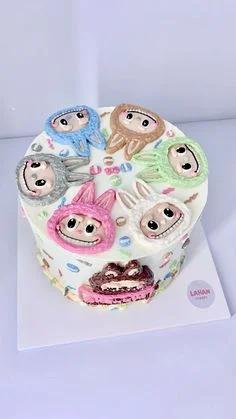 White 1-tier cake featuring multiple colorful character faces in bunny hoods with sprinkles and icing decorations.
