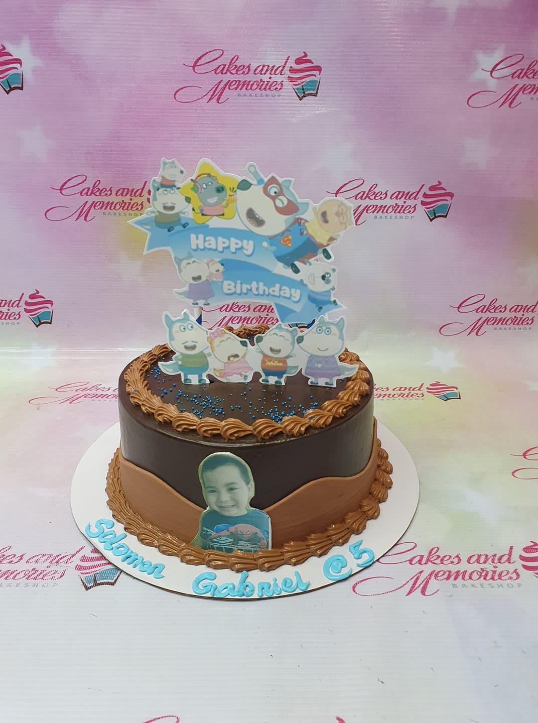 Chocolate birthday cake with blue character printouts and a photo of a boy on the side.