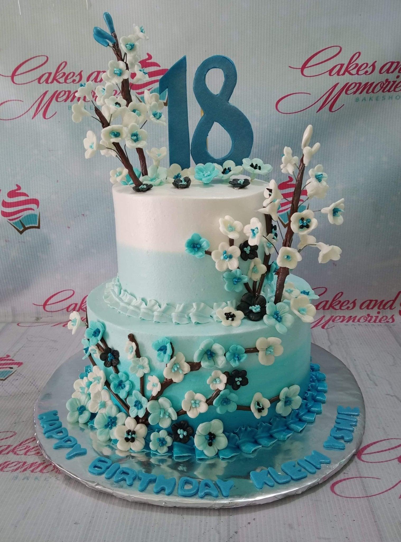 Two-tier light blue and white ombre cake decorated with white and blue cherry blossom branches and a large blue number 18 topper.