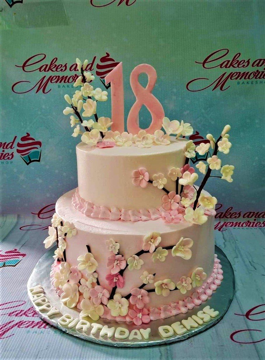 Two-tier pink cherry blossom cake with a large pink number 18 topper and white floral branches.
