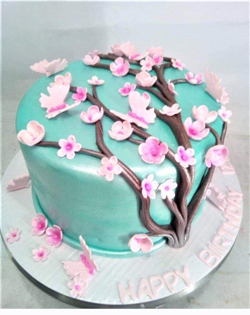 Teal fondant cake decorated with a brown gumpaste cherry blossom tree, pink flowers, and pink butterflies.