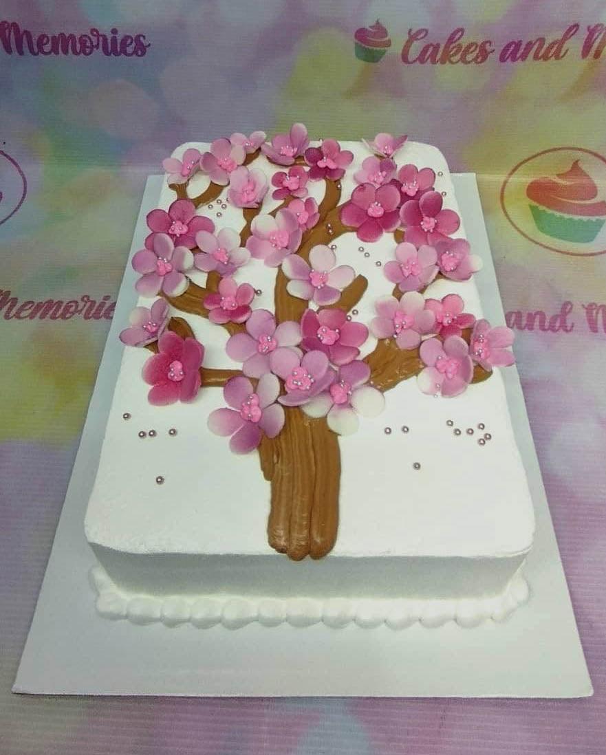 White rectangular cake decorated with a brown icing tree and pink gumpaste cherry blossoms with silver dragees.