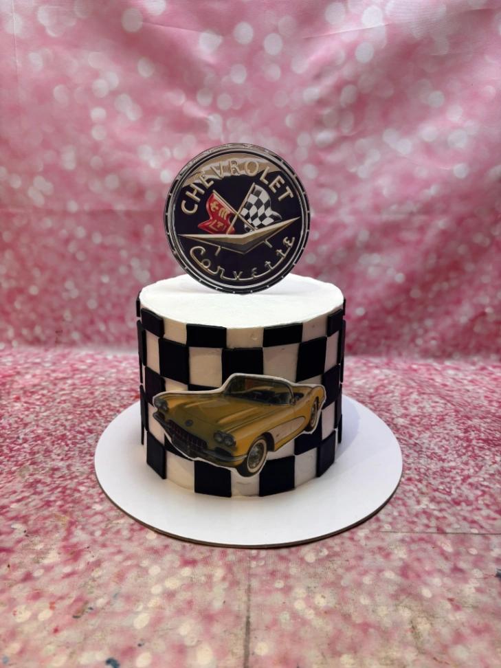 White 1-tier Chevrolet Corvette themed cake with black and white checkered pattern and vintage yellow car printout.