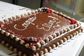 Chocolate rectangle sheet cake with white piped icing message and decorative chocolate and cream rosettes around the border.
