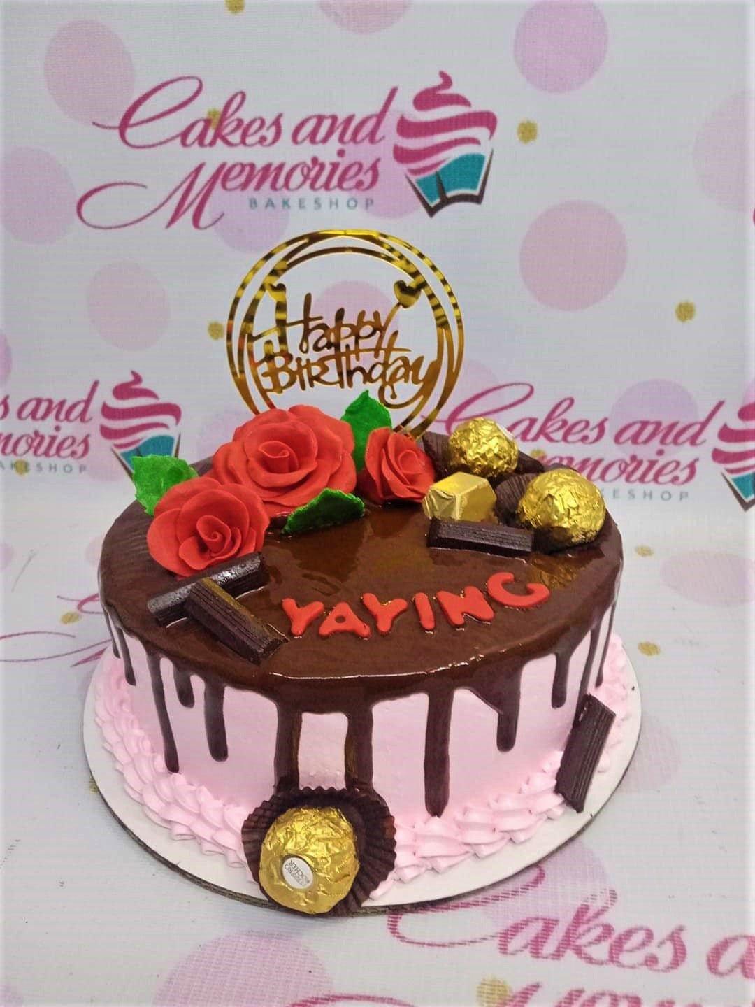 Pink chocolate drip cake with red fondant roses, Ferrero Rocher chocolates, and a gold Happy Birthday topper.