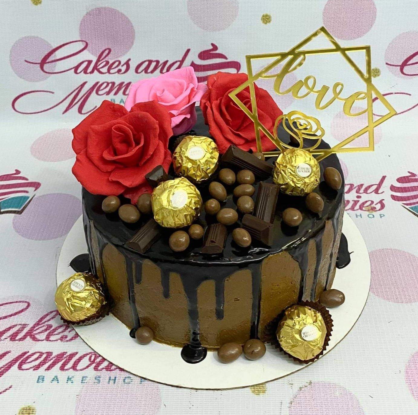 Chocolate drip cake with red and pink roses, Ferrero Rocher chocolates, and a gold Love topper.
