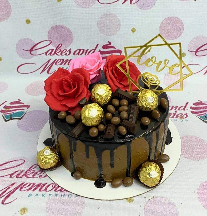 Chocolate drip cake with red and pink roses, Ferrero Rocher chocolates, and a gold Love topper.
