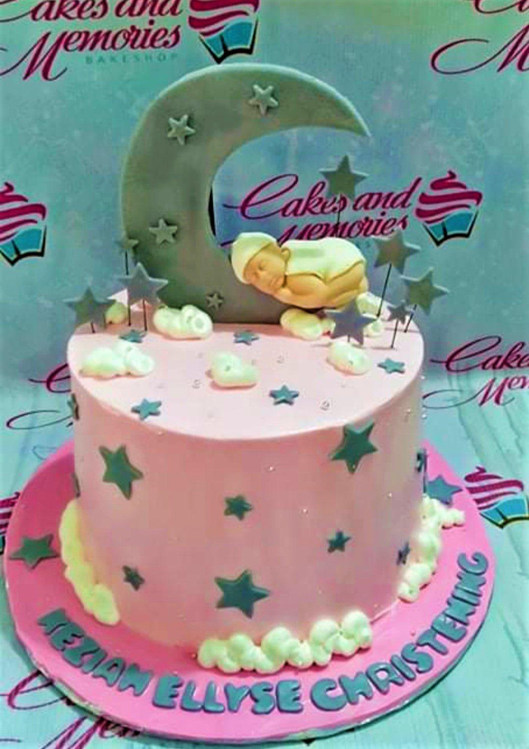 Pink christening cake with a sleeping baby on a large crescent moon topper, surrounded by stars and clouds.