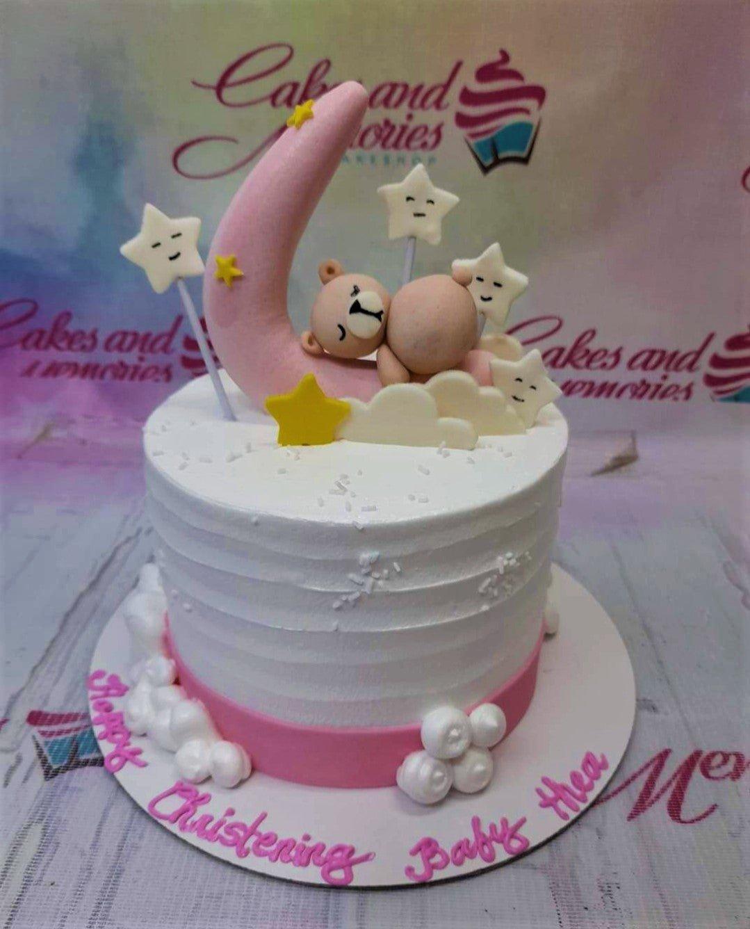 White soft-icing christening cake with a pink fondant moon, sleeping bear, and star toppers on a pink base board.