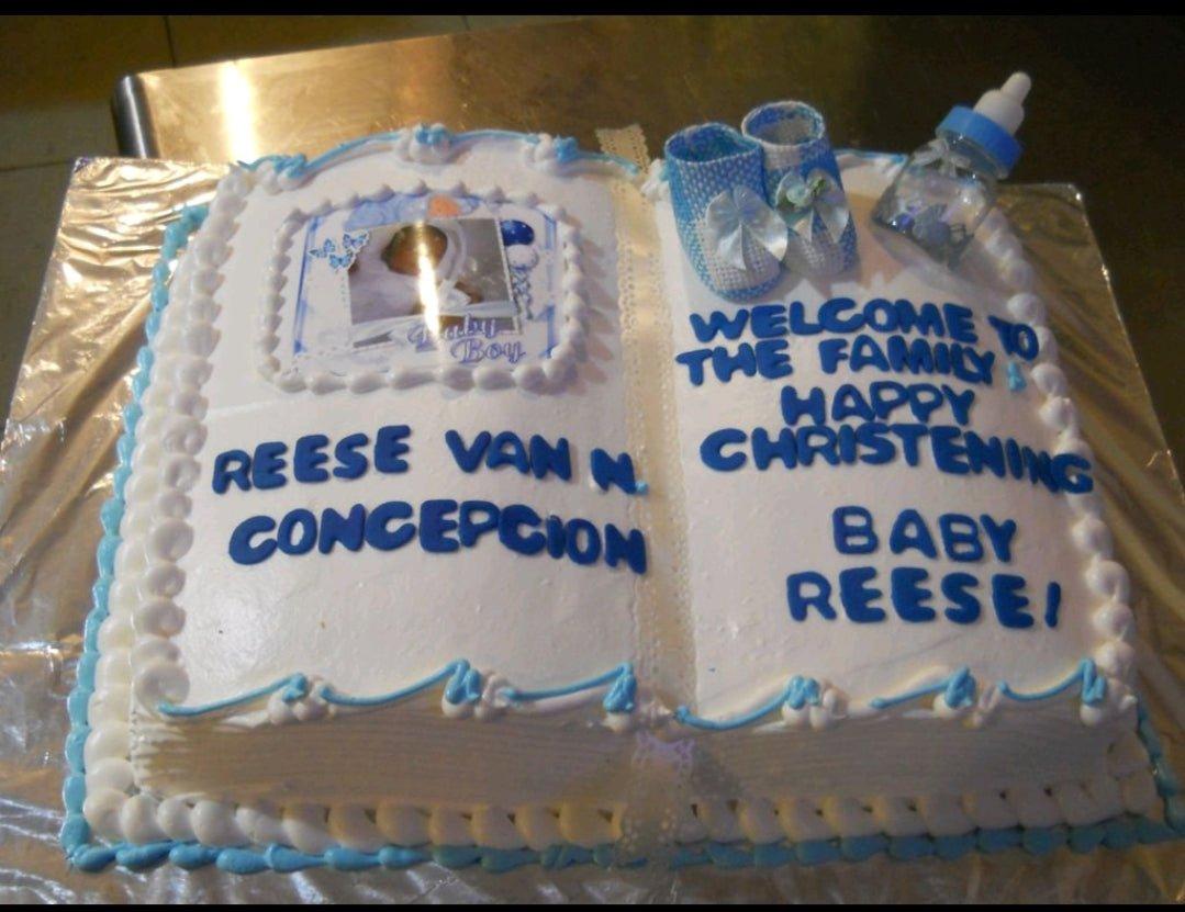 Rectangle christening cake for a baby boy designed as an open book with blue and white icing, a baby photo, and baby shoe toppers.