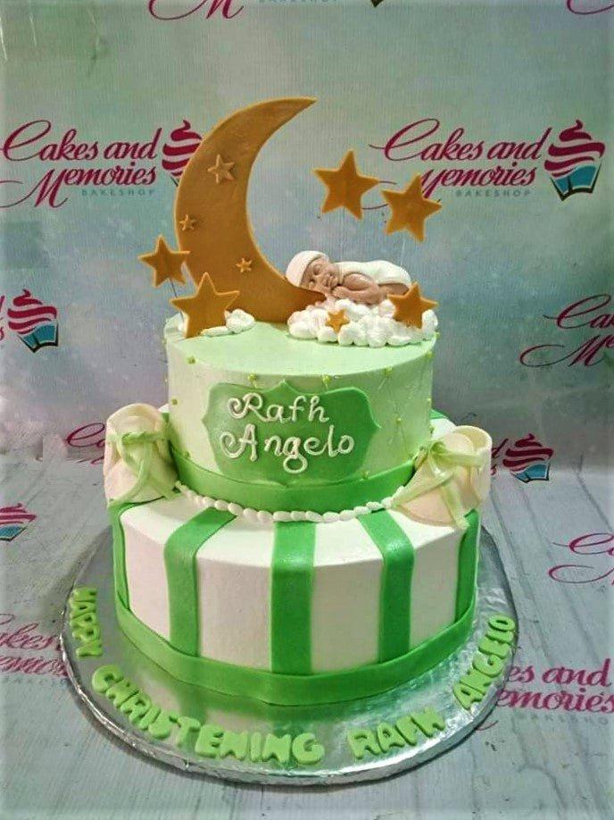 Two-tier green and white christening cake with a sleeping baby on a moon topper and gold stars.