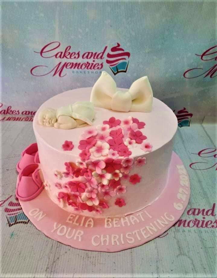 Pink christening cake with a sleeping baby figurine, a large white bow, and cascading pink fondant flowers.