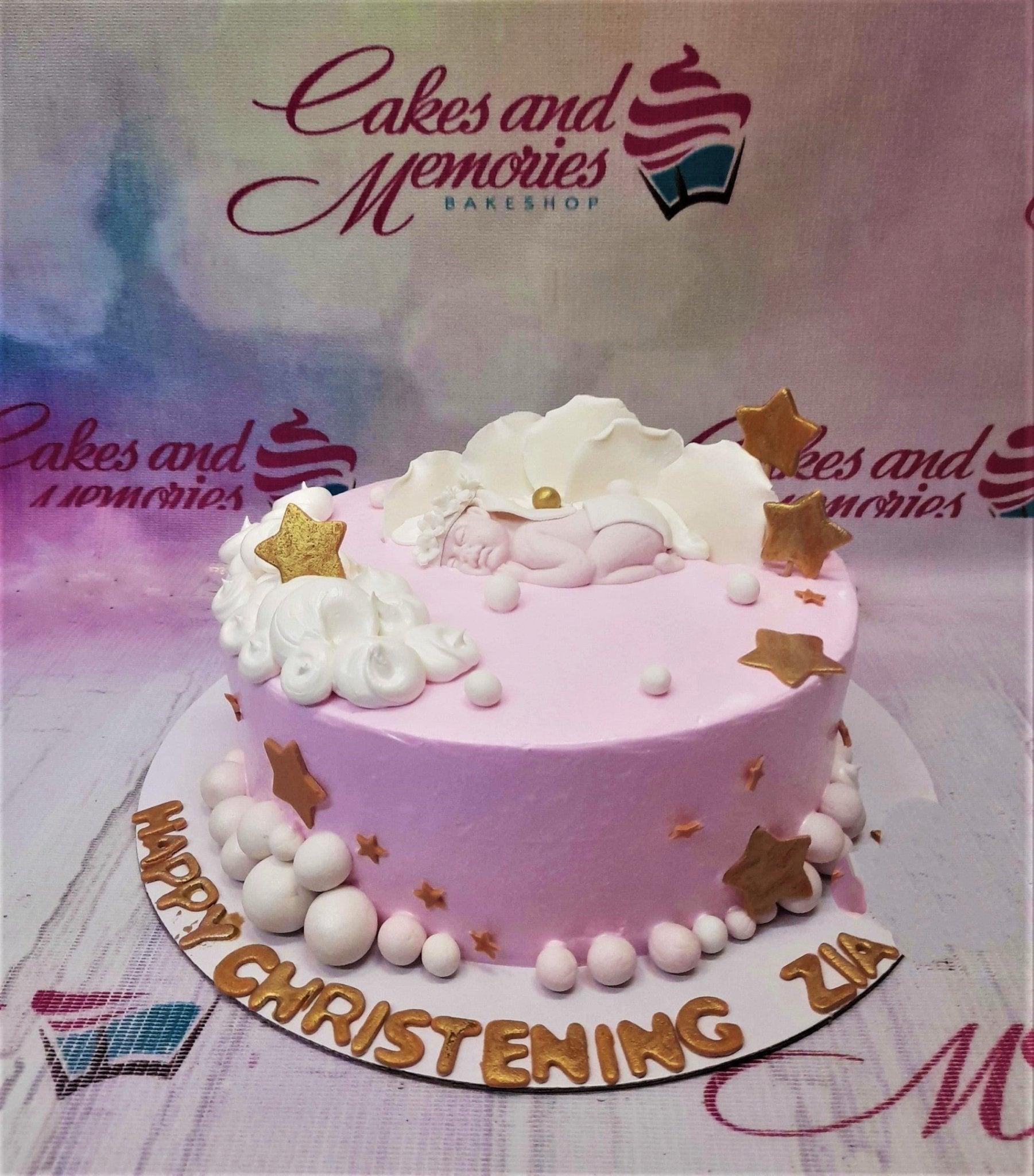 Pink christening cake for Zia featuring a sleeping baby figurine on white icing clouds with gold stars and white pearls.