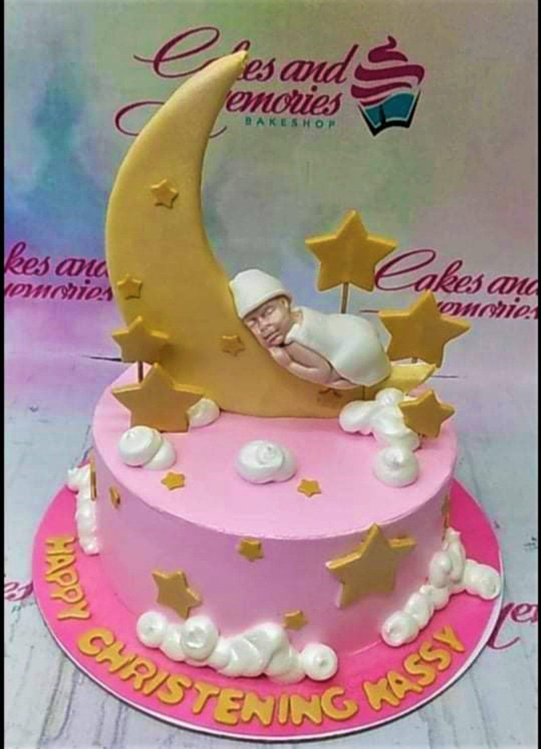 Pink christening cake with a sleeping baby on a gold crescent moon, gold stars, and white icing clouds.