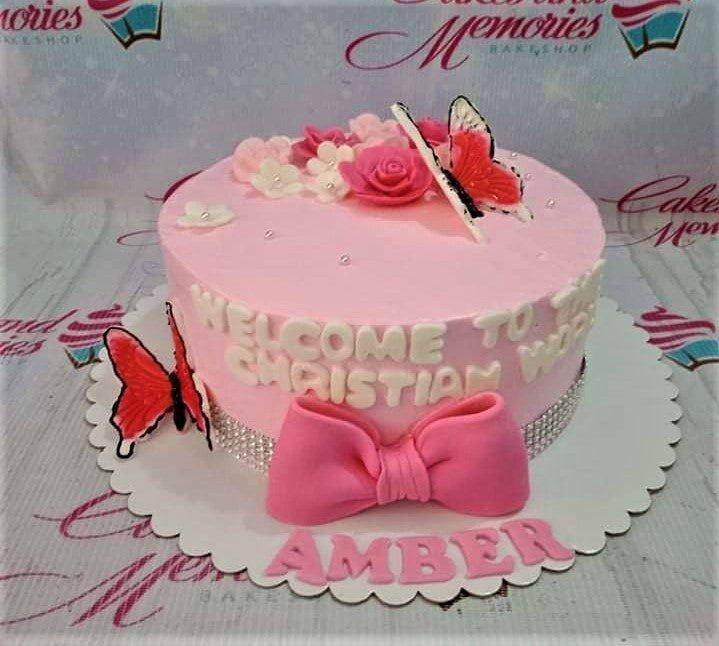 Pink Christianing cake with a large pink fondant bow, butterflies, and edible flowers on a soft pink icing base.