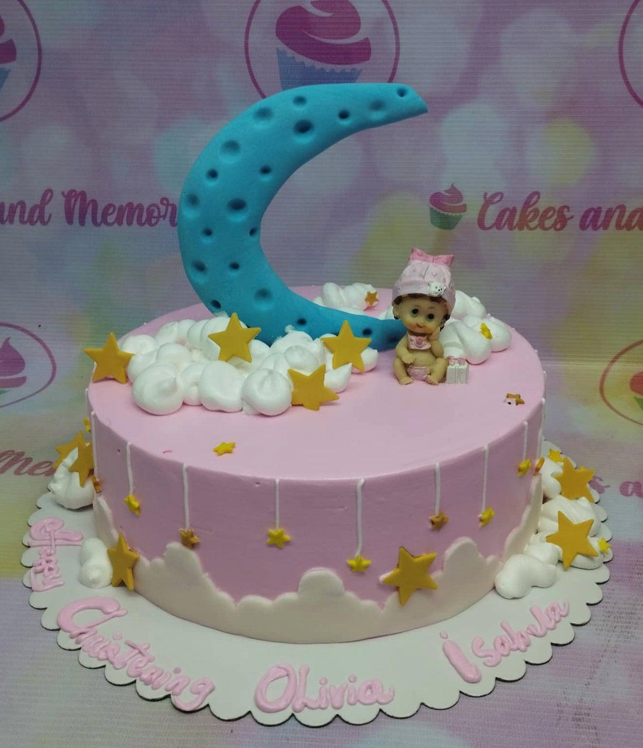Pink christening cake for Olivia Isabela featuring a blue fondant moon, a baby figurine, and yellow stars on a cloud-like icing base.