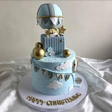 Light blue 1-tier christening cake with a hot air balloon topper, a teddy bear in a basket, gold spheres, and white clouds.
