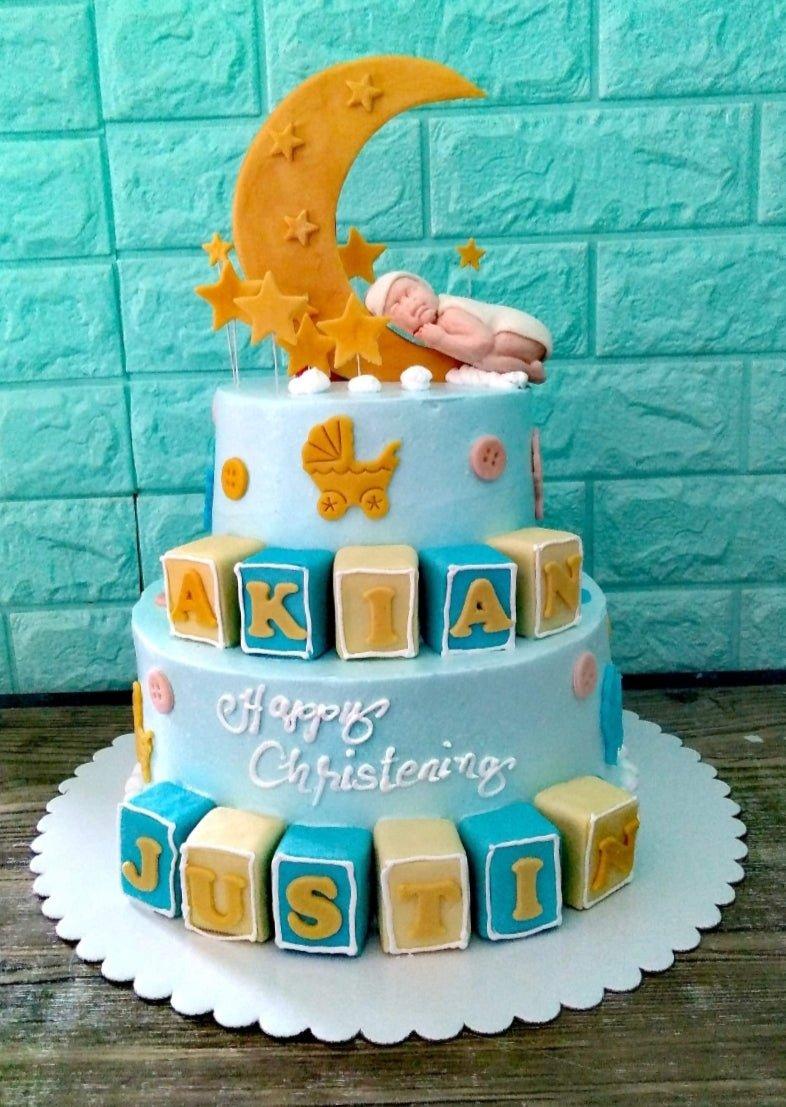 Light blue 2-tier christening cake with a sleeping baby on a crescent moon, yellow stars, and name blocks for Akian Justin.