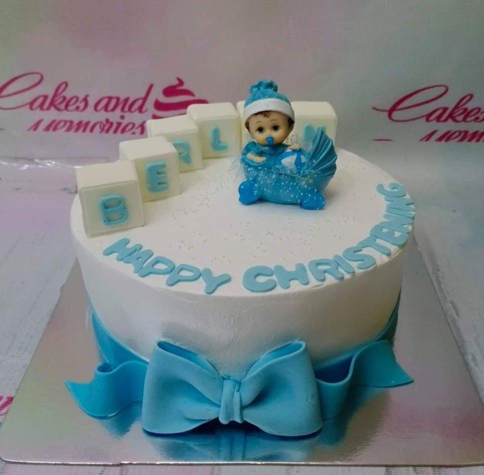 White round christening cake with a blue baby in a stroller topper, blue bow, and block letters spelling BERL.