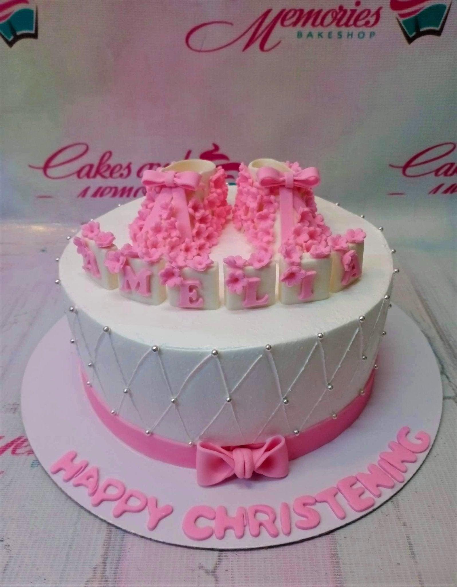 White 1-tier christening cake with pink fondant baby booties, quilted icing pattern, and silver dragees.