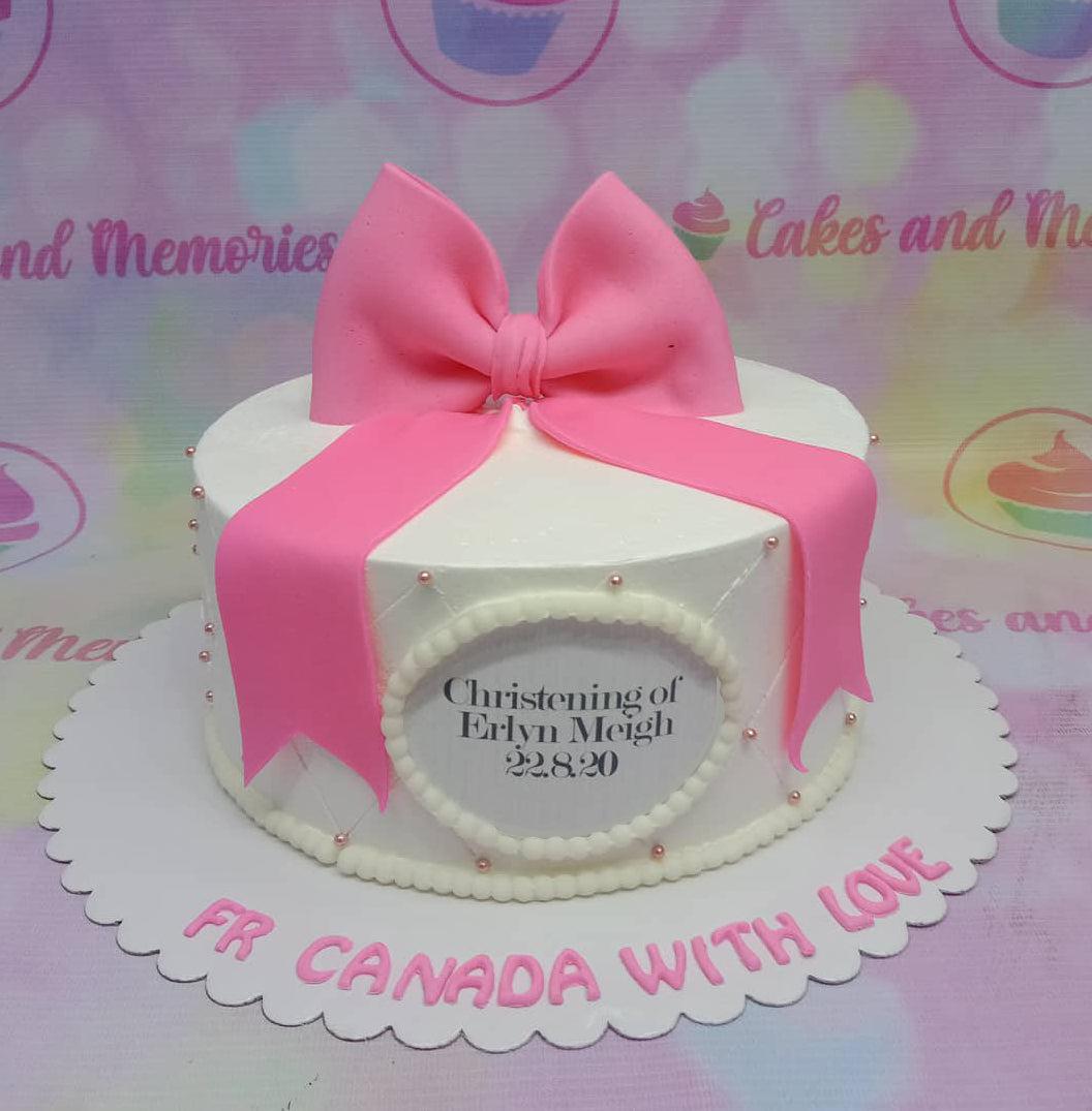 White 1-tier christening cake with a large pink fondant bow, quilted pattern with pink dragees, and a personalized message.