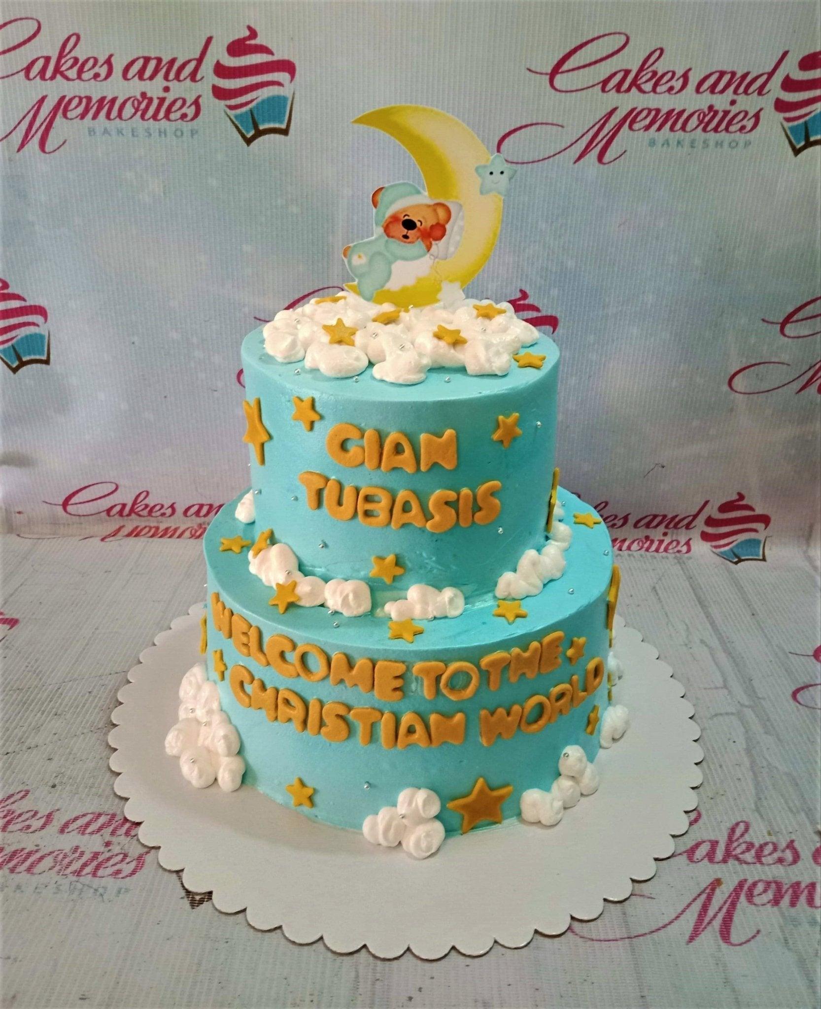 Light blue 2-tier Christian world cake with a sleeping bear on a moon topper, white icing clouds, and yellow fondant stars.
