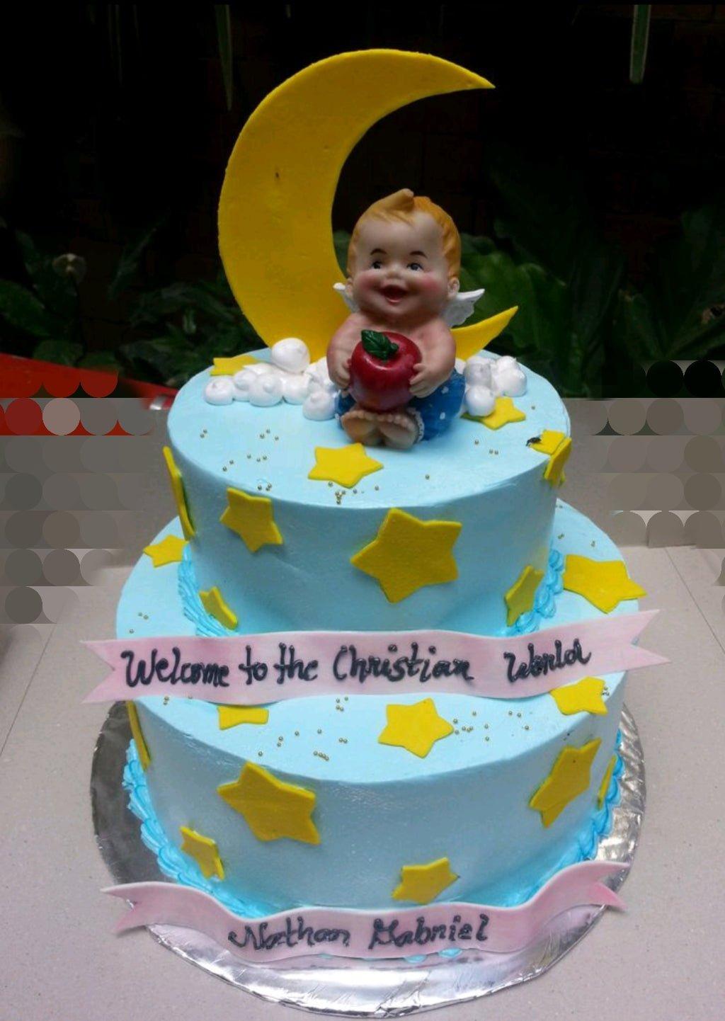Two-tier light blue baptism cake with a large yellow crescent moon, a baby angel figurine, and yellow fondant stars.