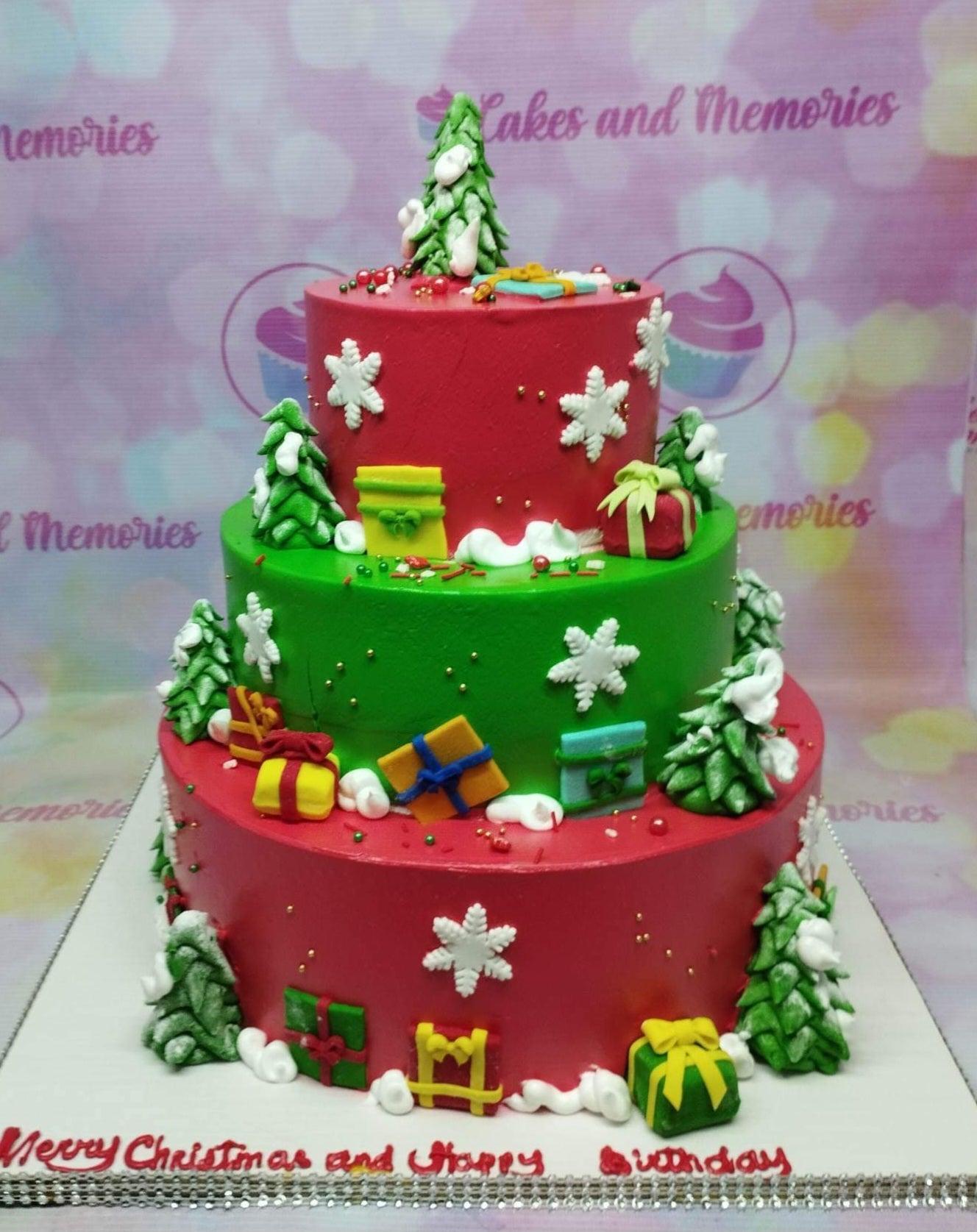 Three-tier Christmas and birthday cake in red and green with fondant trees, gift boxes, and snowflakes.