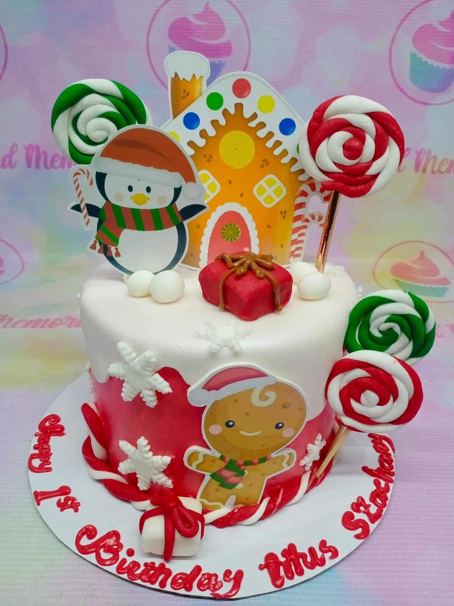 Christmas themed 1st birthday cake with gingerbread house, penguin, and gingerbread man toppers in red and white icing.
