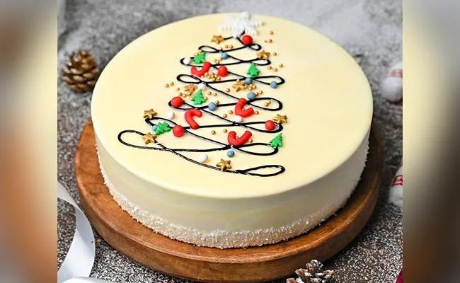 White minimalist Christmas cake with a piped chocolate tree design, colorful ornaments, and a coconut flake border.